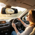 Pet mom smiling as her dog sleeps peacefully in the car mounted bed reflected in the rearview mirror